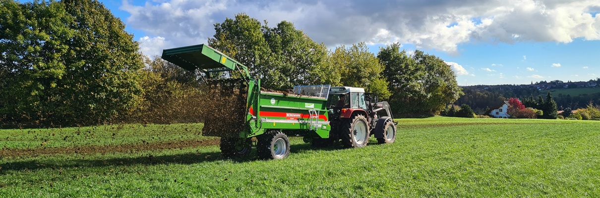 Miststreuer hinter Traktor im Einsatz auf Wiese